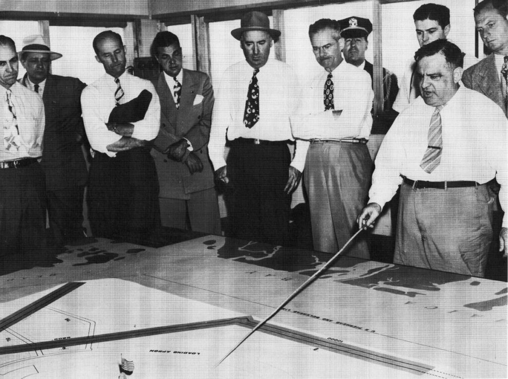Mayor La Guardia in boardroom explaining model of New York International Airport (Idlewild) to businessmen. La Guardia pushed through construction of Idlewild in 1940s. (Cradle of Aviation Museum)