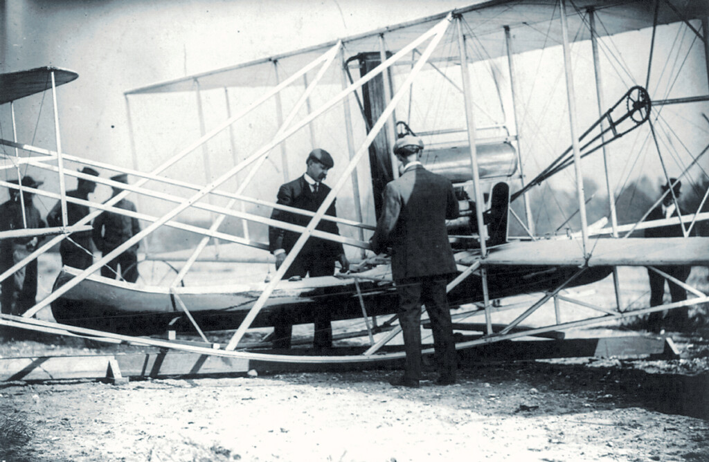 Finding Charlie New York Airport Wilbur Wright examining canoe attachment to aeroplane before 1st flight over water.